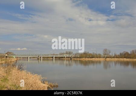 Brücke über einen breiten Fluss und Lagune bei Sonnenaufgang, malerische Wolken am Himmel. Feder. Stockfoto