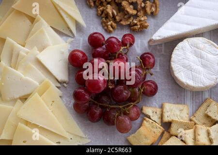Käseplatte mit verschiedenen Arten von geschnittenem und weichem Käse, Trauben, Brot und Nüsse. Käseplatte Draufsicht mit weißem Hintergrund Stockfoto