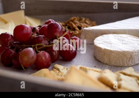 Käseplatte mit Trauben, Nüssen und Brot serviert. Seitenansicht der Stillleben von Käse Stockfoto