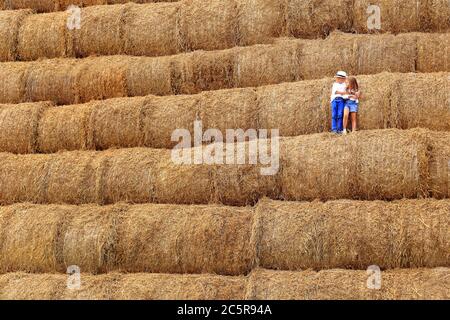 Zwei Kinder stehen in der Heusaison hoch unter dem Himmel auf einem Heuhaufen. Stockfoto