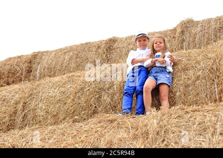 Zwei Kinder stehen in der Heusaison hoch unter dem Himmel auf einem Heuhaufen. Stockfoto