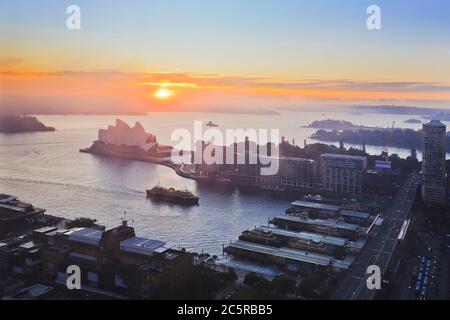Die Sonne geht über dem Hafen von Sydney auf und um die wichtigsten Wahrzeichen der Stadt Sydney am Ufer mit Fähranlegestelle am Circular Quay. Stockfoto