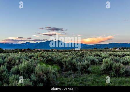 Panoramablick auf Sonnenuntergang und Wüste Salbei Pinsel Pflanzen im Ranchos de Taos Tal und grüne Landschaft im Sommer mit Sonnenlicht auf Wolken Stockfoto