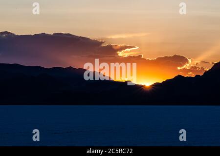 Bonneville Salt Flats dunkelblaue Landschaft in der Nähe von Salt Lake City, Utah und Silhouette Blick auf die Berge und Sonnenuntergang Sonnenstrahlen glühen hinter Wolken Stockfoto