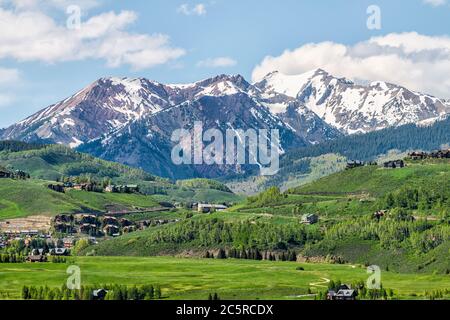 Mount Crested Butte Berggipfel und Dorf im Sommer mit Unterkünften Häuser auf Hügeln mit grünem Gras offenen Hügel und schneebedeckten felsigen Bergen Stockfoto