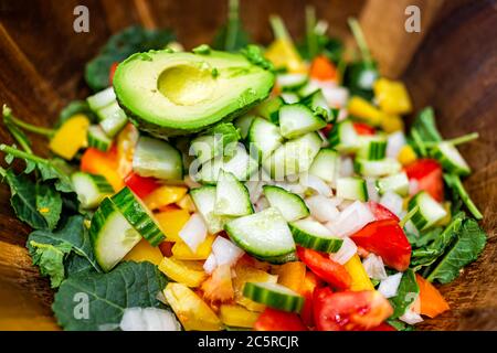 Gehacktes Gemüse in Holzschüssel Makro-Nahaufnahme mit frischem veganen Salat mit Baby Grünkohl, Tomaten, Paprika und Avocado Hälfte Stockfoto