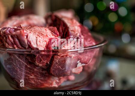 Glas große Schüssel Seitenansicht mit dunklen Blutstückchen von ganzen Rindfleisch rösten rohes rotes Fleisch mit verschwommenem Hintergrund und Textur Zutaten Kochen Stockfoto