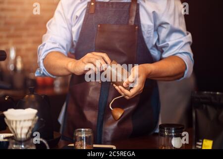 Der Barista gibt Kaffee mit der manuellen Mahlmaschine zum Mahlen von Kaffeebohnen im Café. Stockfoto