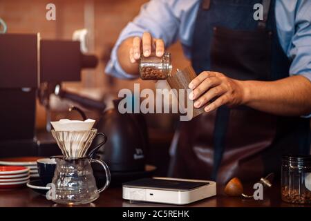 Der Barista gibt Kaffee mit der manuellen Mahlmaschine zum Mahlen von Kaffeebohnen im Café. Stockfoto