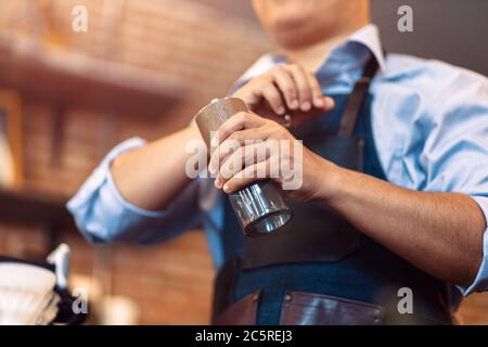 Der Barista gibt Kaffee mit der manuellen Mahlmaschine zum Mahlen von Kaffeebohnen im Café. Stockfoto