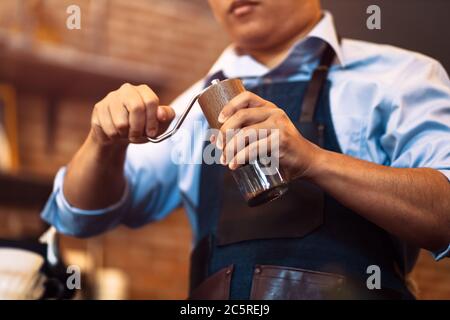 Der Barista gibt Kaffee mit der manuellen Mahlmaschine zum Mahlen von Kaffeebohnen im Café. Stockfoto