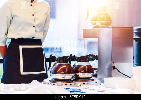 Kellnerin stand neben Kaffeebecher in Gasherd und Kaffeemaschine. Stockfoto