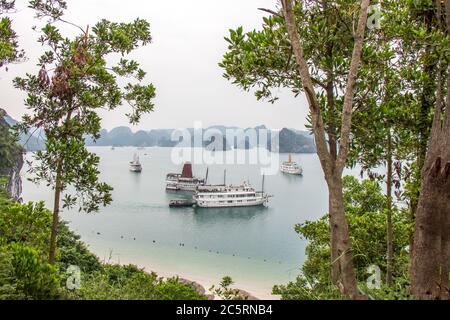 Eine schöne Aussicht auf Trödelboote in der UNESCO-Weltkulturerbe der Ha Long Bay, eine Lücke in den Bäumen Stockfoto