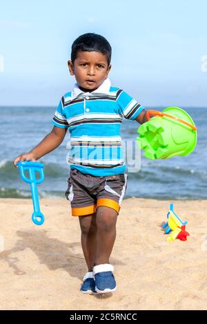 Ein Sri-lankischer Junge, der am frühen Morgen mit einem Plastikeimer und Spaten am Strand von Negombo in Sri Lanka spielt. Stockfoto