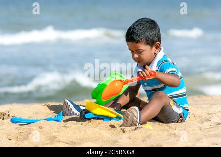 Ein Sri Lanka Junge spielt mit einem Plastikeimer, Schubkarre und Spaten am Negombo Strand in Sri Lanka am frühen Morgen. Stockfoto