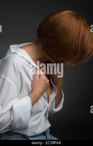 Foto einer reifen Frau auf dunklem Hintergrund in einem weißen Männerhemd mit kurzen roten Haaren Stockfoto