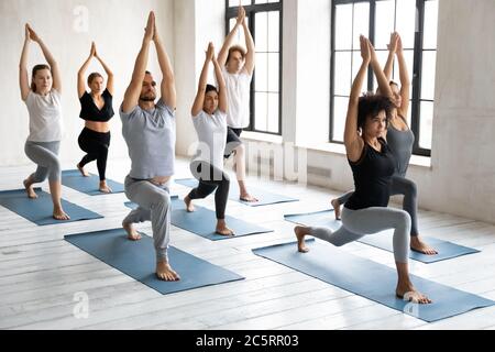 Motivierte fokussierte junge multirassische verschiedene Menschen stehen in virabhadrasana 1 Pose. Stockfoto
