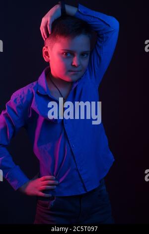 Studio-Portrait eines dunkelhaarigen Jungen, auf dunklem Hintergrund, in einer Kapuzenjacke in der Kapuze. Helle Farbe: Rot und blau Stockfoto