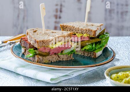 Rindfleisch-Sandwich mit eingelegter Gurke und Senfkartarsauce in zwei Hälften geschnitten Stockfoto