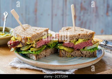 Rindfleisch-Sandwich mit eingelegter Gurke und Senfkartarsauce in zwei Hälften geschnitten Stockfoto