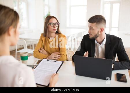 Junge Geschäftsmann mit Laptop und Geschäftsfrau in Brillen nachdenklich Blick auf einander, während im Gespräch mit Bewerber über die Arbeit. Jung Stockfoto