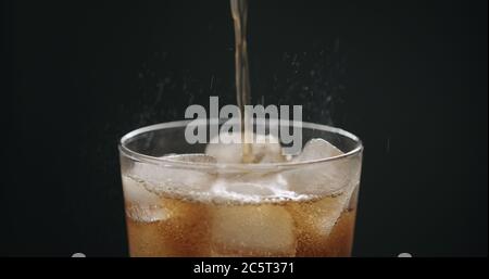 Cola in Glas mit Eiswürfeln auf schwarzem Hintergrund gießen Nahaufnahme Stockfoto