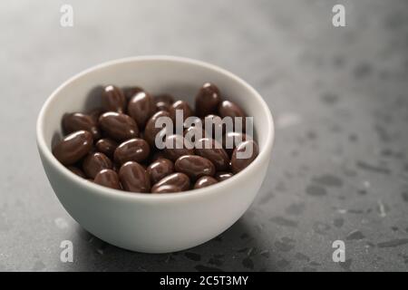 Milchschokolade-Dragee in weißer Schale auf Beton-Hintergrund Stockfoto