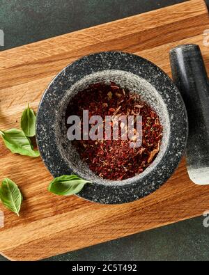 Marmormörtel mit rotem Pfeffer, Basilikumblättern und getrockneten Tomaten auf Holzbrett. Von oben aus Blick auf Gewürze. Stockfoto