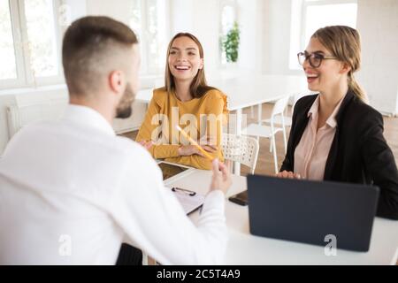 Zwei schöne Geschäftsfrauen glücklich im Gespräch mit männlichen Bewerber für die Arbeit. Junge lächelnde Arbeitgeber verbringen Job Interview im Büro Stockfoto