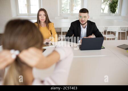 Junge Geschäftsmann in Brillen mit Laptop und Geschäftsfrau nachdenklich im Gespräch mit Bewerber über die Arbeit. Interview mit jungen Arbeitgebern, die Arbeit ausgeben Stockfoto