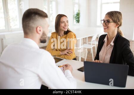 Zwei fröhliche Geschäftsfrauen glücklich im Gespräch mit männlichen Bewerber für die Arbeit. Junge lächelnde Arbeitgeber verbringen Job Interview im Büro Stockfoto