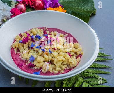 Gnocchi mit Karottencreme und Kornblume. Teller mit Malbenblüten verziert. Blumenfutter Konzept. Essbare Sommerblumen Stockfoto