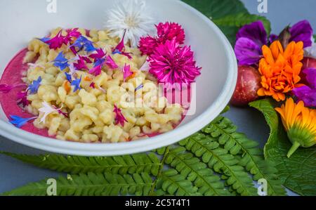 Gnocchi mit Karottencreme und Kornblume. Teller mit Malbenblüten verziert. Blumenfutter Konzept. Essbare Sommerblumen Stockfoto