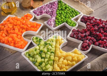 Rohes Gemüse Karotten, Erbsen, Zwiebeln, Gurken, Kartoffeln, in Würfel geschnittene Rüben liegen auf Platten, die in Puzzles gesammelt werden. Stockfoto