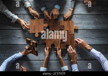 Business People Team sitzen um den Besprechungstisch und Montage von Holz Puzzle-Stücke Einheit Zusammenarbeit Ideen Konzept Stockfoto