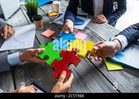 Das Team der Geschäftsleute sitzt am Besprechungstisch und montiert farbige Puzzleteile über Finanzdatenberichte Stockfoto