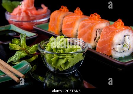 Japanisches Essen. Eine Reihe von verschiedenen Rollen von Lachs, Aal, Garnelen und rotem Kaviar, in einer schönen grünen Schüssel, auf einem schwarzen Hintergrund mit Reflexion. Stockfoto