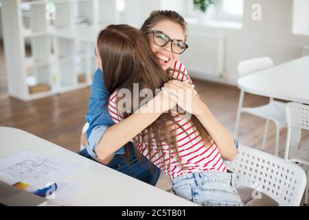 Zwei hübsche lächelnde Mädchen umarmen sich während der Arbeit. Fröhliche Frauen arbeiten freudig im modernen Büro Stockfoto