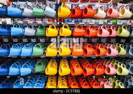 Reihen von bunten Tassen hängen auf dem Regal zum Verkauf in einem Supermarkt, handgefertigte Keramik, Teekannen und Geschirr zum Verkauf Stockfoto