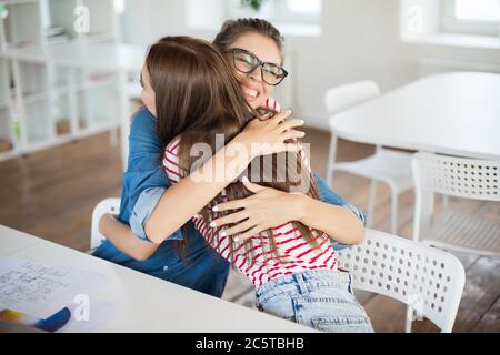 Zwei schöne Mädchen glücklich umarmt einander während der Zeit bei der Arbeit. Fröhliche Frauen arbeiten freudig im modernen Büro Stockfoto