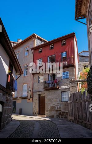 Guimarães, Portugal - schöne erhaltene mittelalterliche bunte traditionelle Steinhäuser mit Holzfenstern und kleinen Balkonen und Blumentopf Stockfoto