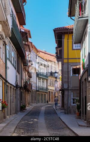 Guimarães, Portugal - schöne erhaltene mittelalterliche bunte traditionelle Steinhäuser mit Holzfenstern und kleinen Balkonen und Blumentopf Stockfoto