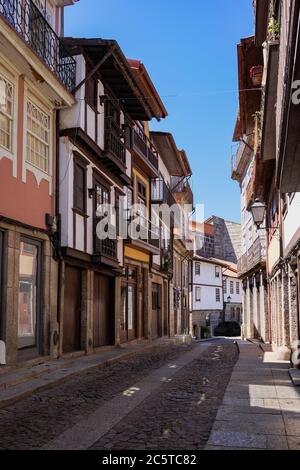 Guimarães, Portugal - schöne erhaltene mittelalterliche bunte traditionelle Steinhäuser mit Holzfenstern und kleinen Balkonen und Blumentopf Stockfoto