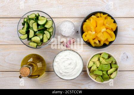 Zutaten in Scheiben für rohes Gurkensuppenpüree: griechischer Joghurt, Gurke, Avocado, gelber Paprika und Knoblauch auf einem Holztisch. Rohkost. Stockfoto