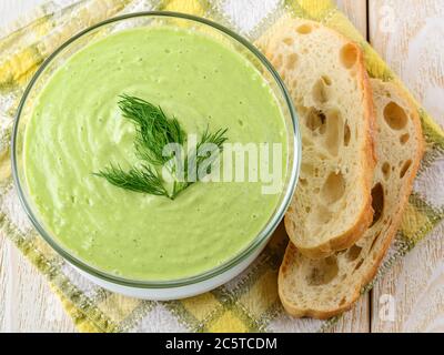 Frisches, kaltes Gurkensuppenpüree in einer Glasschüssel und Brot auf einem weißen Holztisch. Rohkost Diätsuppe aus griechischem Joghurt, Gurke, Avocado, Paprika. Stockfoto