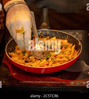 Ein Koch mit Handschuhen kocht Fusilli-Pasta in einer Pfanne Stockfoto