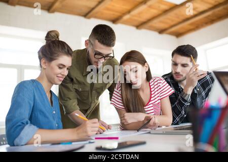 Gruppe von Geschäftsleuten träumerisch mit Skizzen arbeiten, während Zeit bei der Arbeit. Junge kreative Menschen diskutieren gemeinsam neues Projekt Stockfoto