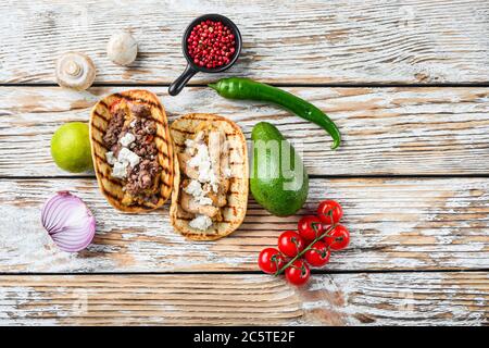 Hausgemachtes Taco mit Huhn und Rindfleisch in der Nähe von rohen Zutaten über weiß strukturierten alten Tisch, Draufsicht mit Platz für Text. Stockfoto