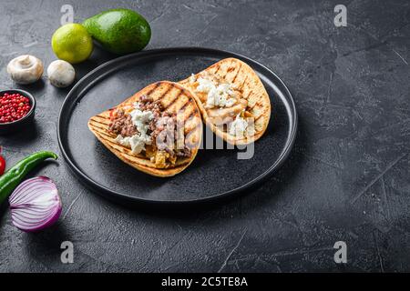 Traditionelle mexikanische Taco mit Huhn und Rindfleisch mit Zutaten eine Seite auf schwarzem Teller über schwarz texturierten Hintergrund Seitenansicht, selektive Fokus mit Stockfoto