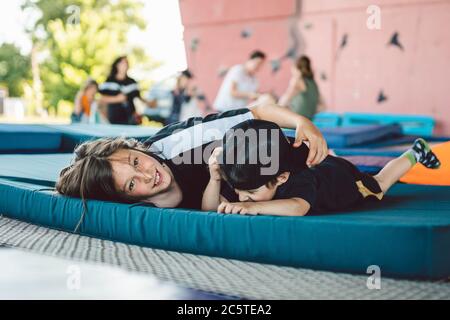 Glückliche Kinder spielen auf Trampolin liegen. Brüder haben Spaß auf einer Sportmatte auf einem Trampolin im Fitnessstudio draußen liegen. Jungs verwöhnen, lachen und Stockfoto